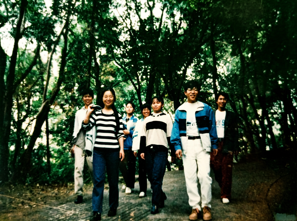 AI enhanced repair of an old class group photo from three decades ago. Erase scratches, dust spots, and color degradation seamlessly. Enhance clarity for every individual in the crowd without altering their true appearances or merging faces. Preserve authentic expressions, natural lighting, and retro school background aesthetics. Masterpiece, ultra-detailed.