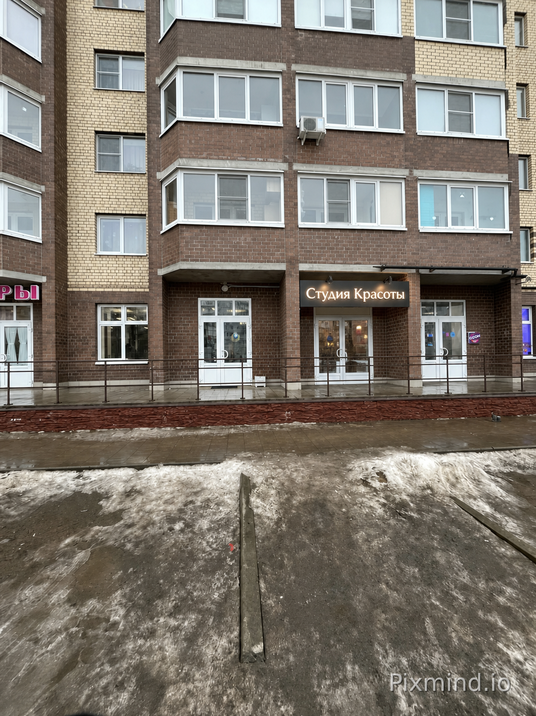 EDIT the supplied original commercial retail storefront photograph. This is an architectural photo edit, not a new storefront concept.

Image 1 is the original storefront photograph whose geometry must be preserved.

PRESERVE: Keep the original camera position, perspective, crop, building outline, floor levels, entrance location, doors, windows, columns, neighboring context, and overall scene geometry unchanged.

SCOPE: Modify only the existing signboard area. Keep the facade finish, doors, windows, pavement, neighboring shops, and surroundings unchanged.

SIGNAGE: Remove the old sign wording and replace it with exactly "Студия Красоты". The replacement text must be crisp, centered, correctly spelled, and fully legible. Use a horizontal signage panel, 3D illuminated letters, and LED lighting.

DESIGN: modern commercial storefront; match the dominant color tones from the reference image palette; modern facade.

Photorealistic commercial architectural visualization, accurate materials, natural reflections, realistic shadows, crisp edges, and a buildable sign design.

CONSTRAINTS: Do not create a different building or move architectural openings. No mockup frames, before-and-after collage, watermarks, annotations, measurements, or unrelated text.